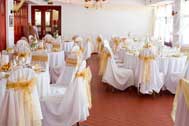 Wedding reception with white covered chairs decorated with gold sash bows 