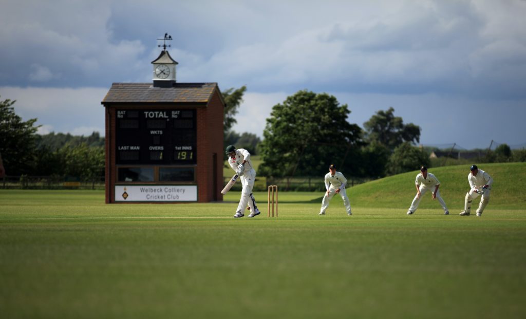 4 cricket players in white on a cricket green